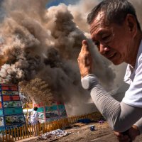 A volunteer shields himself from heat as smoke rises from cremations during the Lang Pacha ceremony at the Dhamma of Buddha Nakhon Ratchasima Foundation complex, Nakhon Ratchasima, Thailand, April 23, 2025. (AFP Photo)