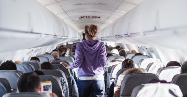 Interior of an airplane with passengers on seats and a traveler walking the aisle. (Shutterstock Photo)